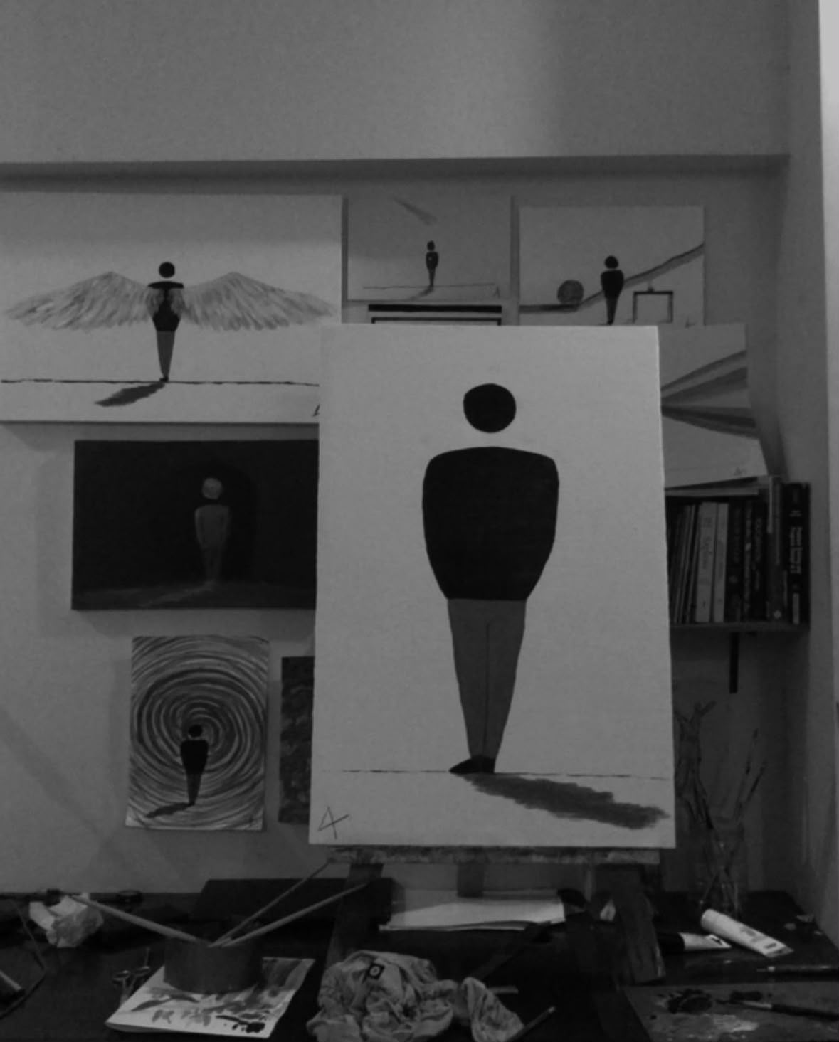 A black-and-white studio photograph of a solitary figure and its shadow on a canvas, surrounded by related paintings.